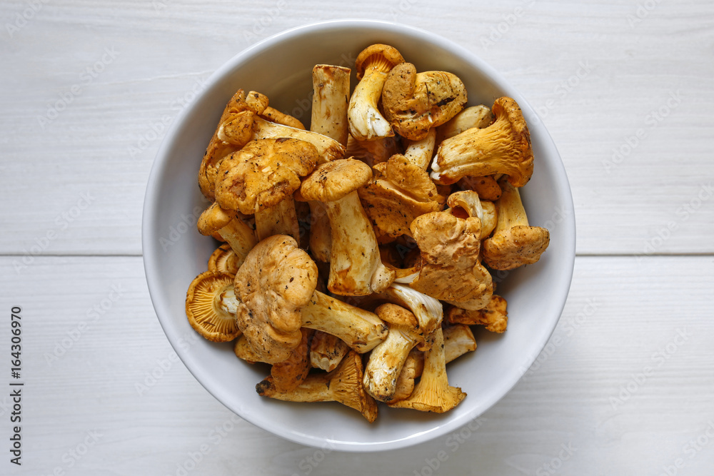 Freshly harvested chanterelle mushrooms in a bowl on white wooden background Freshly harvested chanterelle mushrooms in a bowl on white wooden background