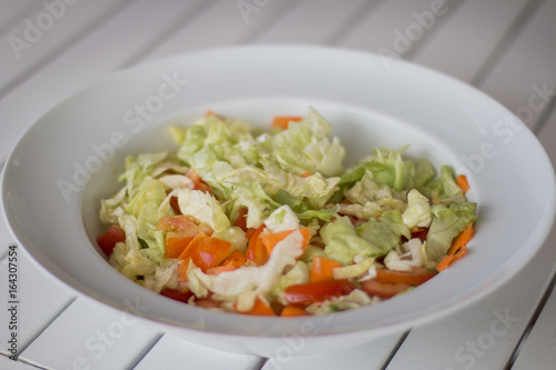 A white plate with tomatoes, carrot, cucumber and lettuce.