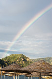Rainbow in the sky against the background of high rocks and mountains on the beach. 