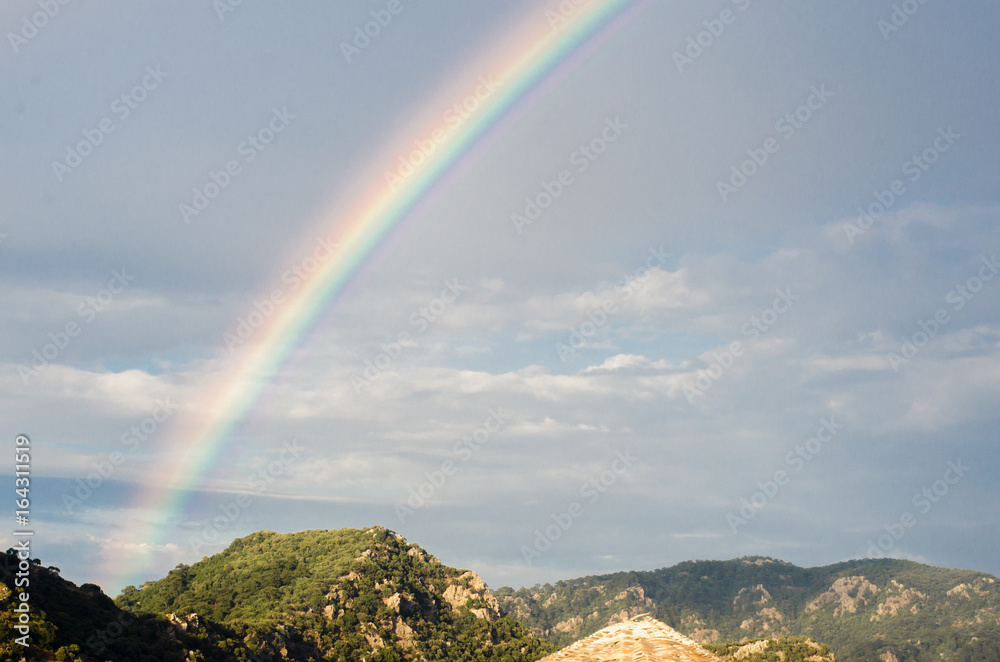 Rainbow in the sky against the background of high rocks and mountains on the beach. 