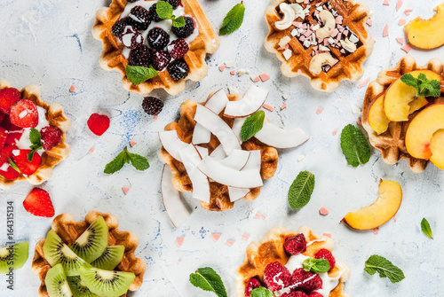 Set of fresh Belgian soft wafers with different toppings - peach, blackberries, raspberries, strawberries, coconut, cashews, strawberries, mint. Light table. top view