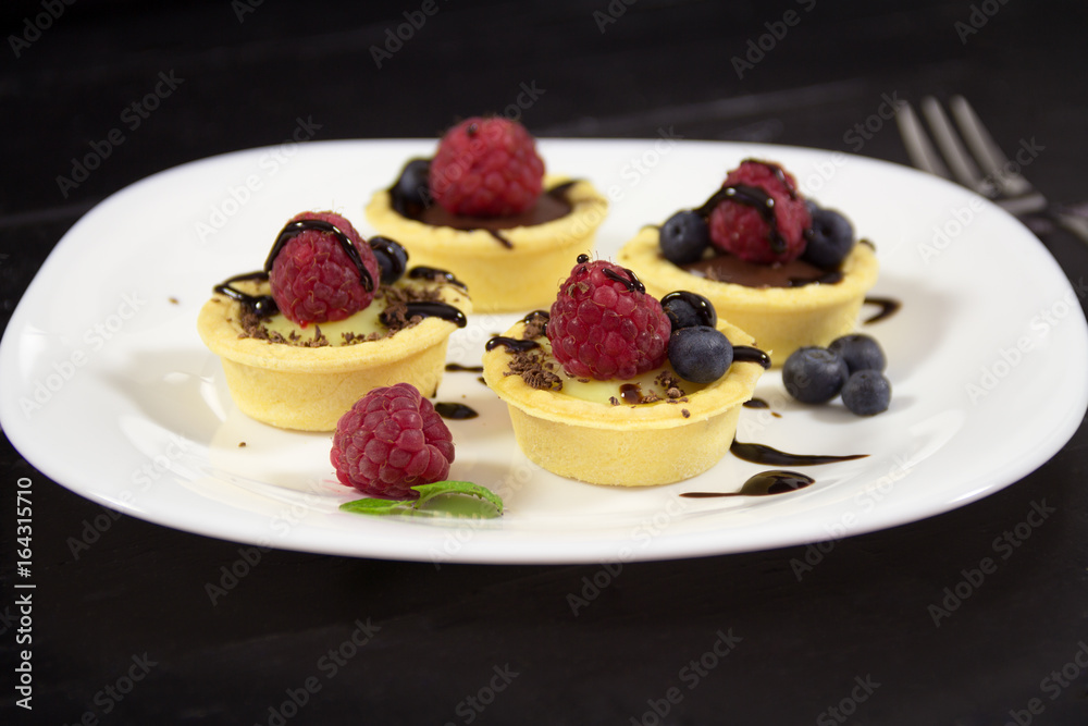 A delicious dessert with vanilla and chocolate pudding in a basket on the white plate with fresh raspberries and blueberries. Light summer sweets A delicious dessert with vanilla and chocolate pudding in a basket on the white plate with fresh raspberries and blueberries. Light summer sweets