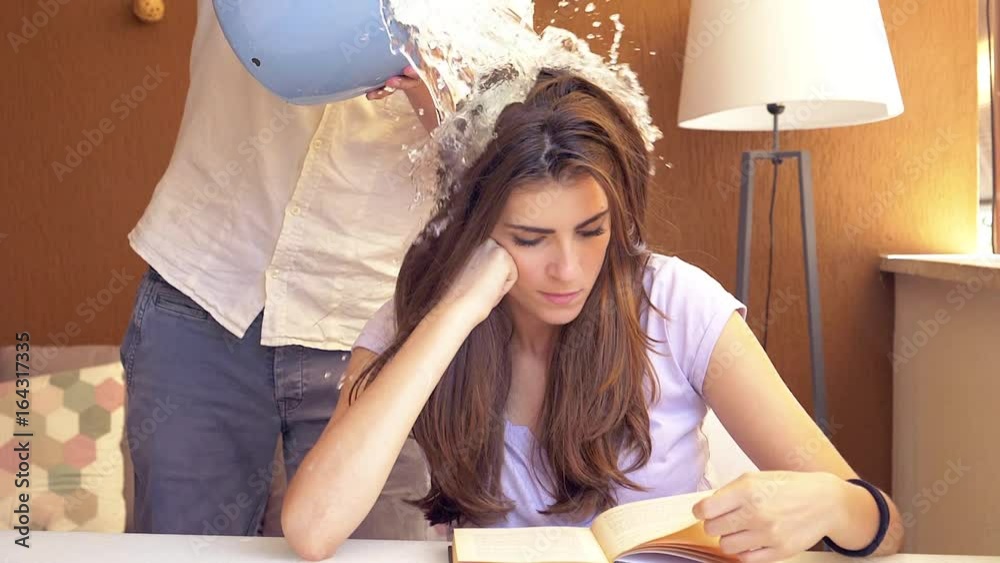 Man making joke to girlfriend splashing bucket of cold water on head closeup super slow motion