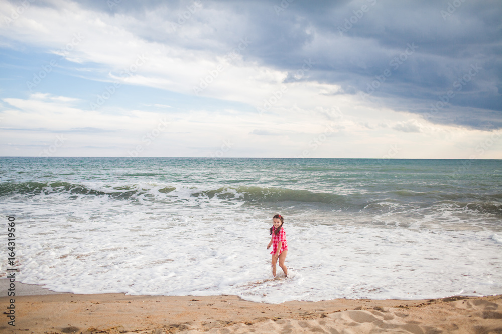  young girl in shirt plays with the surf and stand in waves