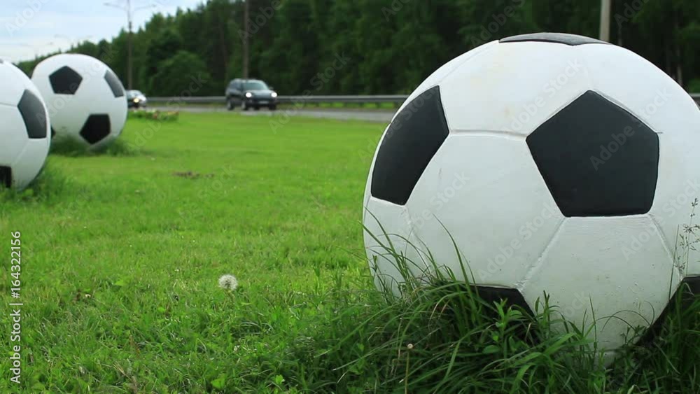 three big soccer balls on the green lawn by the road Stock Video