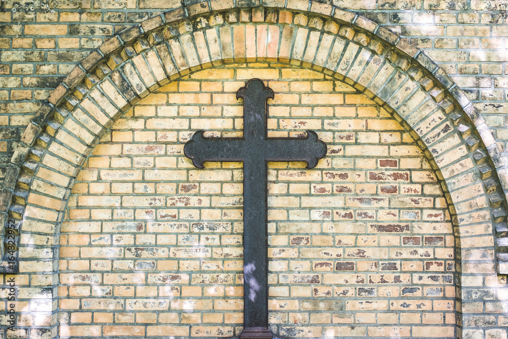 old metal cross on brick wall background , rusty cross on grave