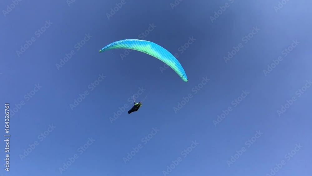 türkisfarbener Paragleiter / Gleitschirm kreist im blauen Himmel durch die Lüfte