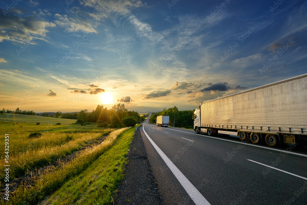 Trucks driving towards the setting sun on a tarmac road in rural countryside