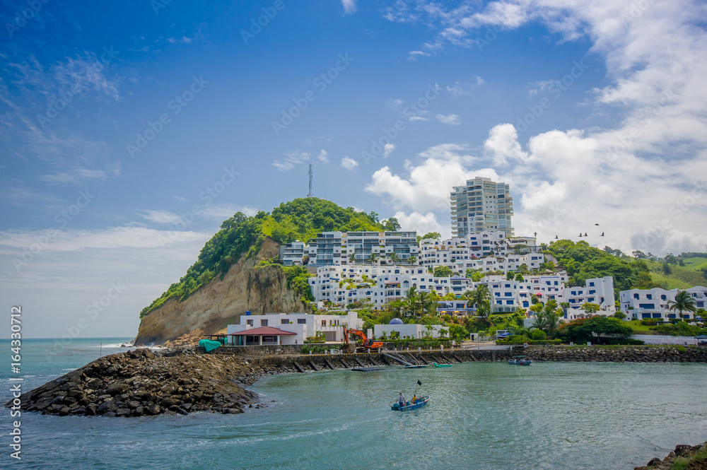 Naklejka premium Beautiful rocky beach with a buildings structure of hotels behind in a beautiful day in with sunny weather in a blue sky in Same, Ecuador
