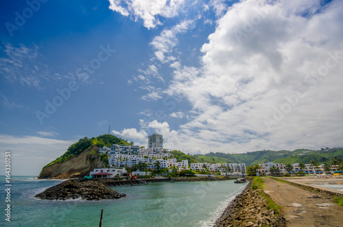 Close up of a rocky beach and buildings behind in a beautiful day in with sunny weather in a blue sky in Same, Ecuador