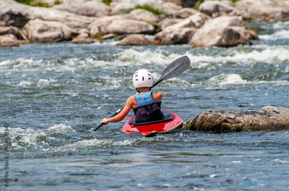 Obraz premium A teenager trains in the art of kayaking. Slalom boats on rough river rapids. The child is skillfully engaged in rafting.