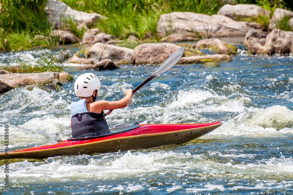 A teenager trains in the art of kayaking. Slalom boats on rough river rapids. The child is skillfully engaged in rafting.