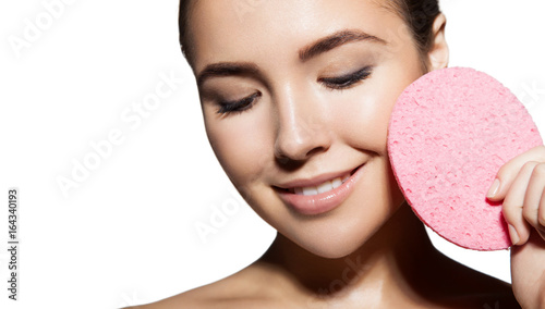Close-up face of young woman with healthy radiant skin with cleansing sponge in hands. Isolated on white background