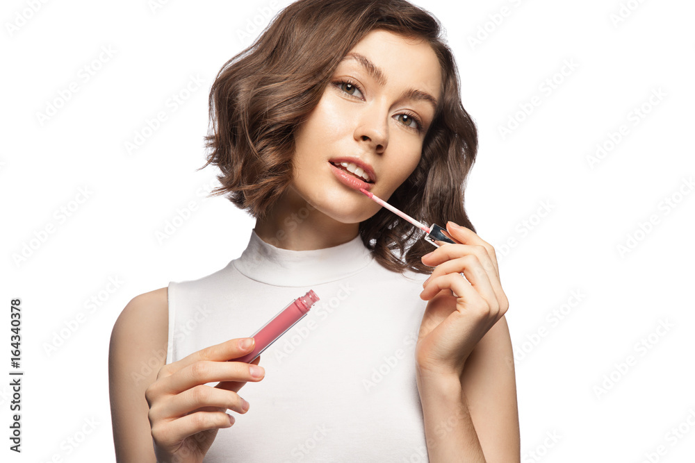 Beautiful woman with natural make-up and short stylish haircut, puts pink lip gloss on white background Beautiful woman with natural make-up and short stylish haircut, puts pink lip gloss on white background