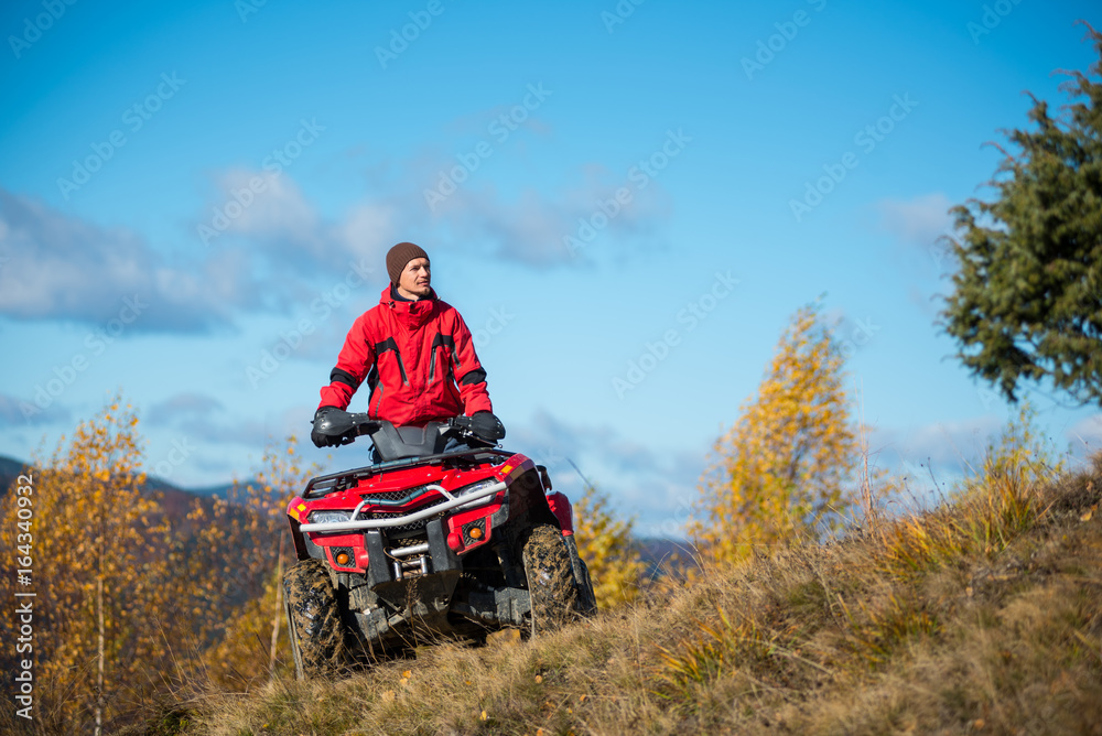 Fototapeta premium Bottom view. A man on the red ATV quad bike against blue sky in the autumn landscape nature. Copy space