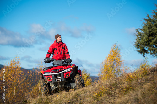 Bottom view. A man on the red ATV quad bike against blue sky in the autumn landscape nature. Copy space