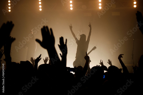 Lit silhouettes of musicians on the smoky stage raising up hand with crowd