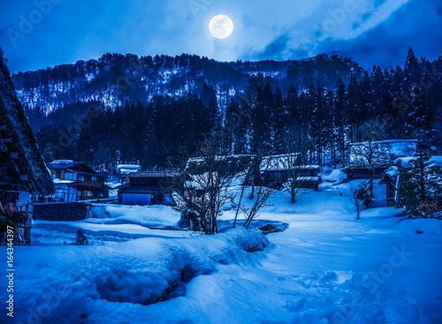 Snow covered the ground in winter. Town with night sky and full moon.