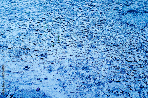 Rain drops on the surface of a street road on a rainy day, toned blue