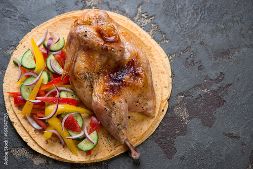 Tortillas with roast halved chicken and fresh vegetables, horizontal shot on a brown stone surface with copy space