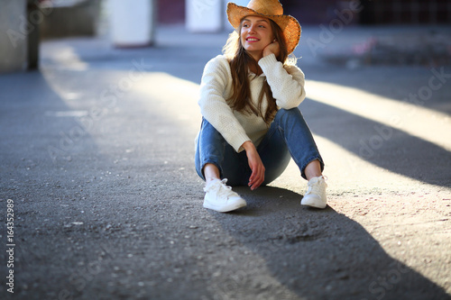 Smiling woman teenage, sitting on asphalt, outdoor, sunlight, street style, casual