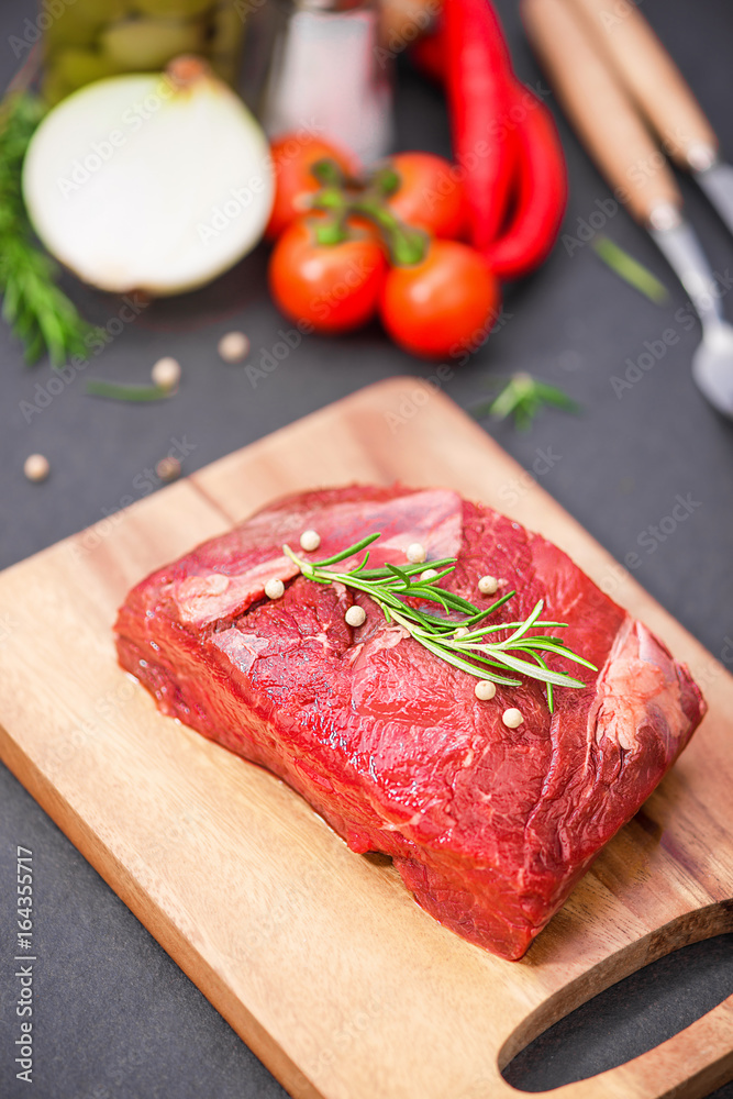Raw beef on a cutting board with spices and ingredients for cooking. Raw beef on a cutting board with spices and ingredients for cooking.