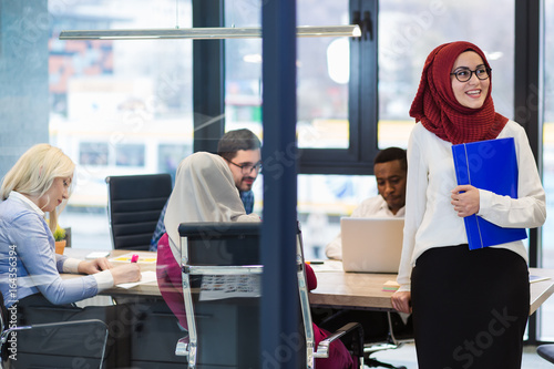 Arabian Businesswoman in office with Businesspeople meeting in the background, Arabian woman wearing Hijab in office with her colleagues in background