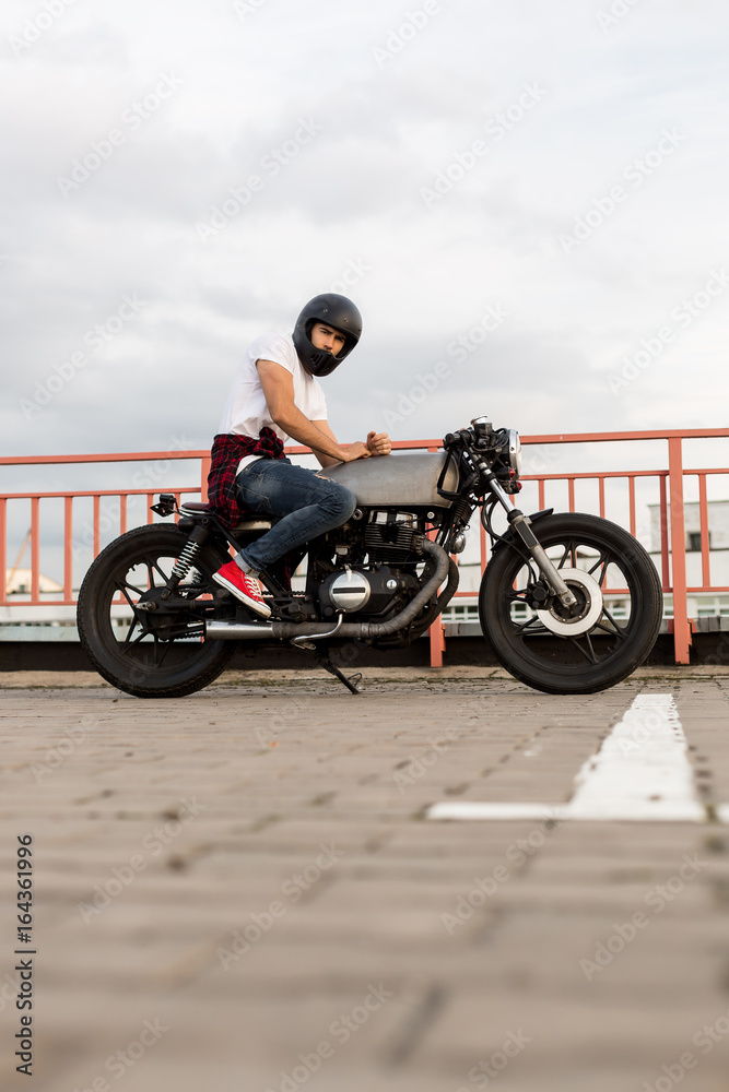 Handsome happy rider guy in red sneakers and black moto helmet look to  camera sit on