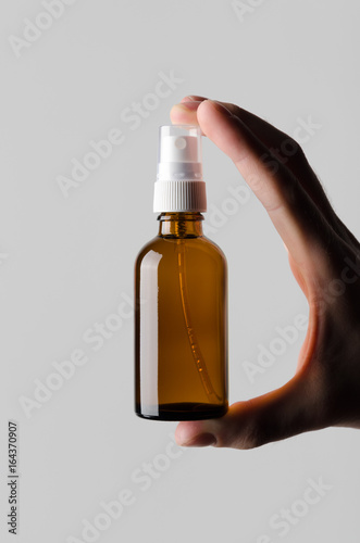 Amber Spray Bottle Mock-Up - Male hands holding an amber spray bottle on a gray background