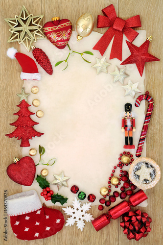 Christmas background border with bauble decorations, mince pie, foil wrapped chocolates, holly and mistletoe on parchment paper oak wood.