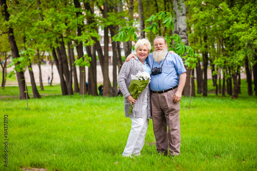 An elderly couple in love stands together in a park with flowers © aemstock