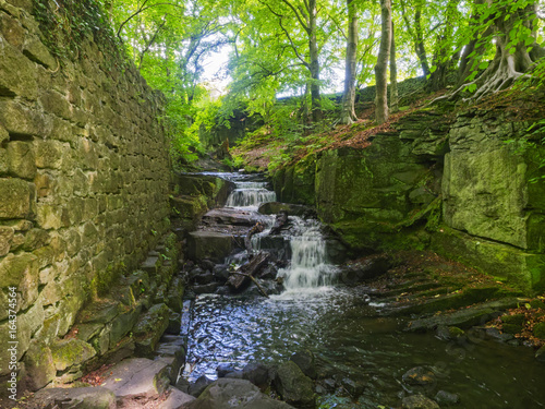Bentley Brook passes between the  sandstone wall of a derelict mill and rocky outcrop through the mill wheel pit.
