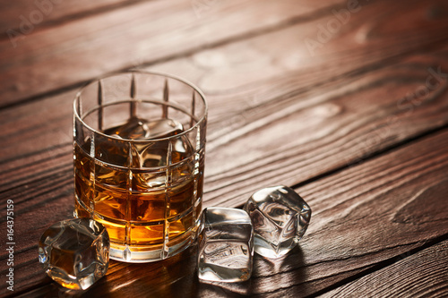 Fotografie Glass of whiskey with ice cubes on wooden table