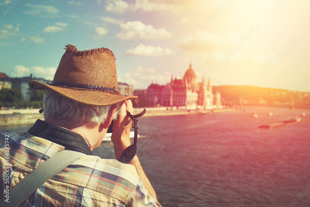 Pensioner tourist in hat capturing Hungarian Parliament building at Budapest