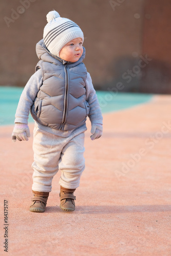 Toddler child in warm vest jacket outdoors. Baby boy at playground during sunset.