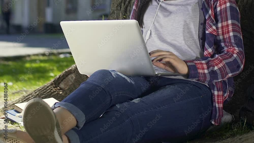 Female student sitting with laptop in university garden, chatting online Female student sitting with laptop in university garden, chatting online