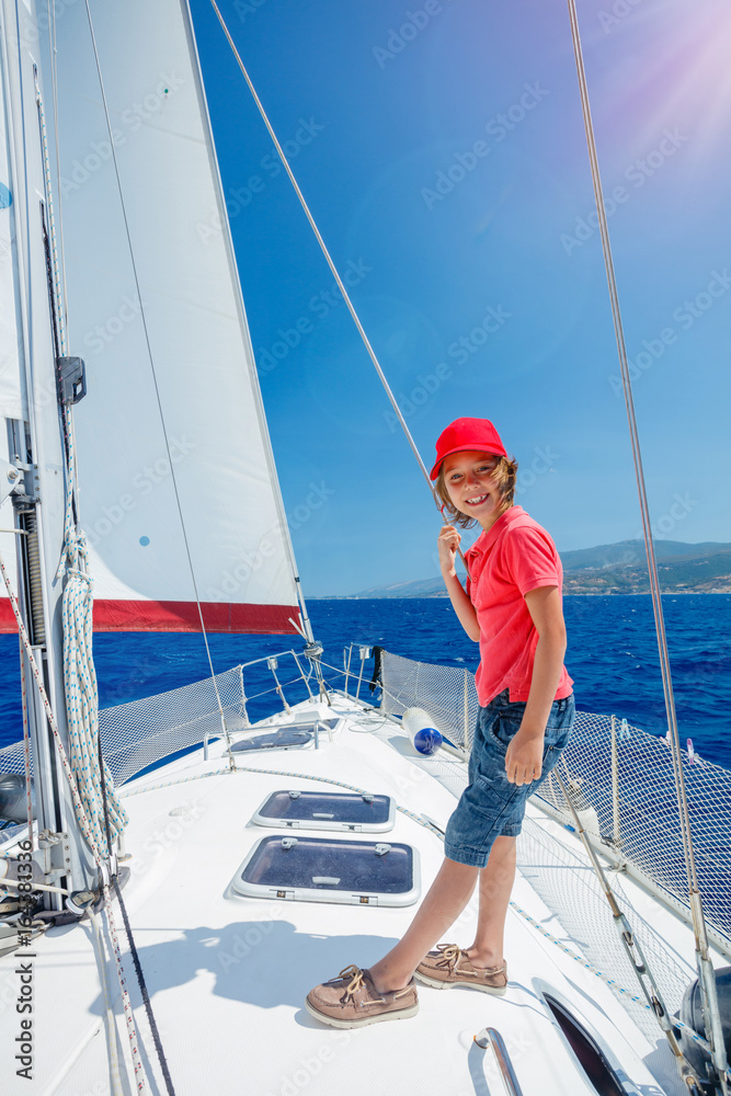 Fototapeta premium Little boy on board of sailing yacht on summer cruise. Travel adventure, yachting with child on family vacation.