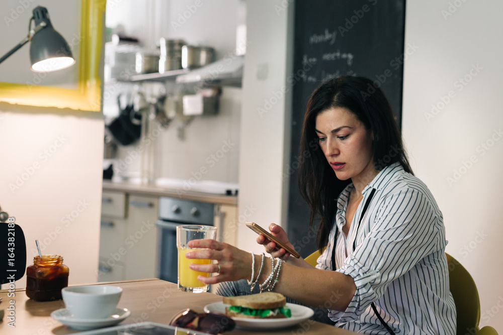Young woman texting message while having breakfast at her home Young woman texting message while having breakfast at her home