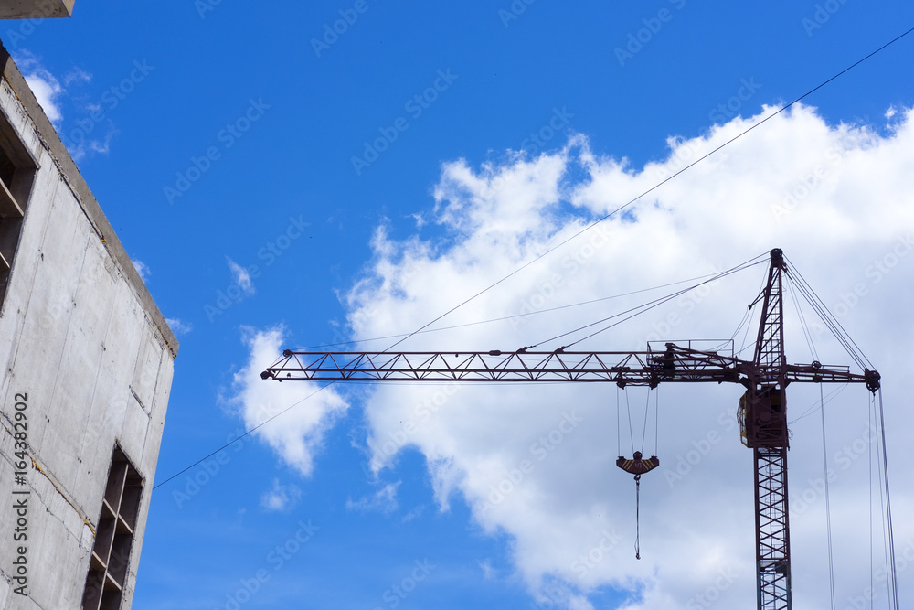 Construction site in the city, crane and the incomplete building on blue sky