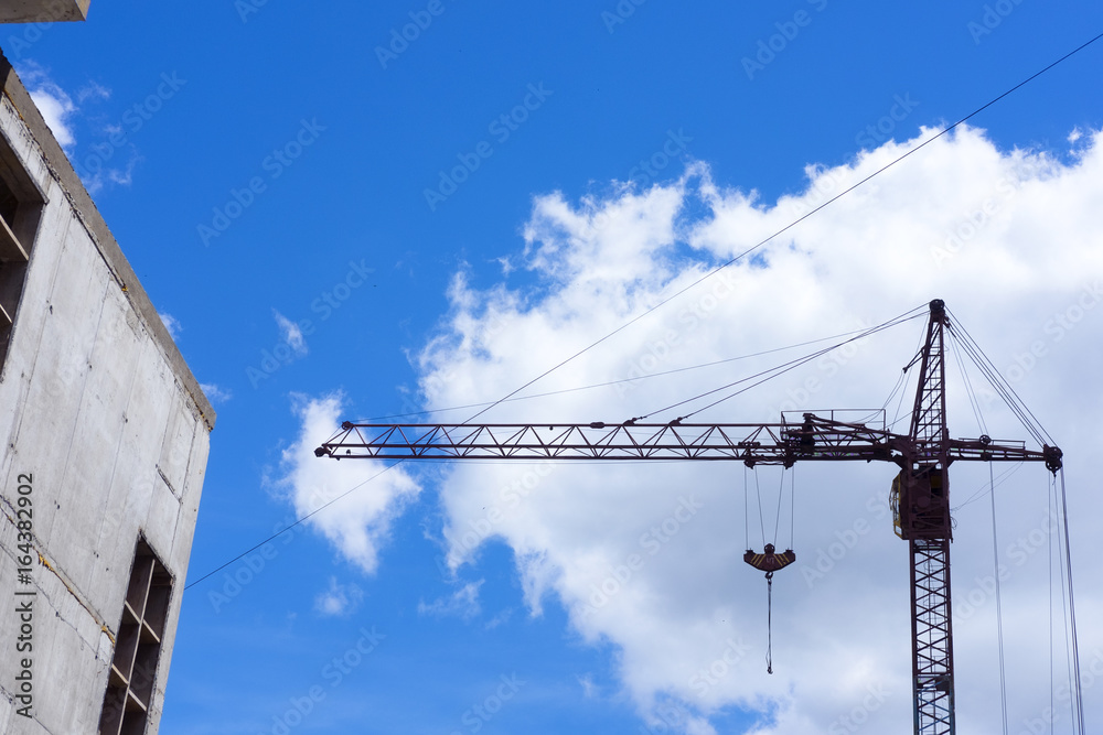 Construction site in the city, crane and the incomplete building on blue sky Construction site in the city, crane and the incomplete building on blue sky