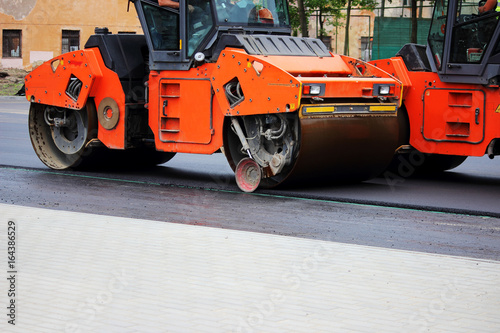 Two heavy compactor tires the upper layer of asphalt in the construction of a parking lot for tourist buses.