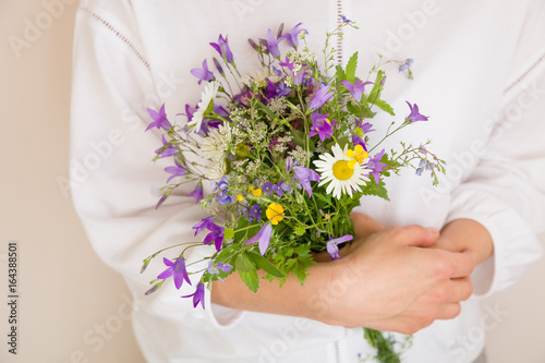 Fototapeta Naklejka Na Ścianę i Meble -  Closeup of woman's hands holding beautiful bunch of wild flowers. Girl with summer bouquet at white wall