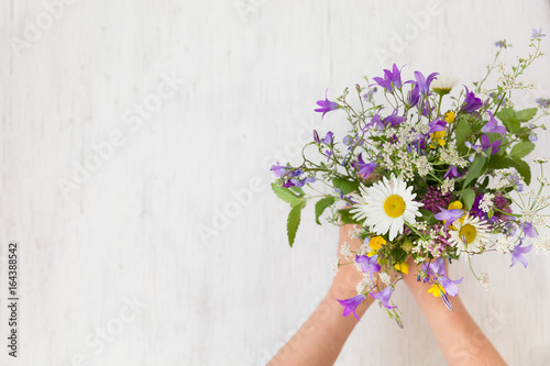 Vászonkép Beautiful bunch of wild flowers in woman's hands on the white wooden background