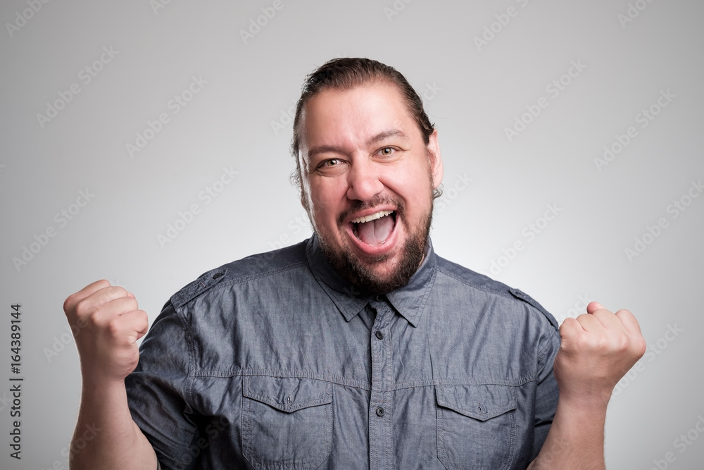 I won Happy young man gesturing and smiling while standing against gray background I won Happy young man gesturing and smiling while standing against gray background