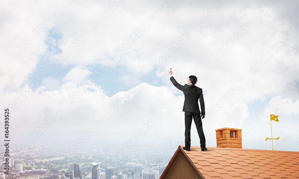 Businessman on house roof touch empty space. Mixed media Businessman on house roof touch empty space. Mixed media