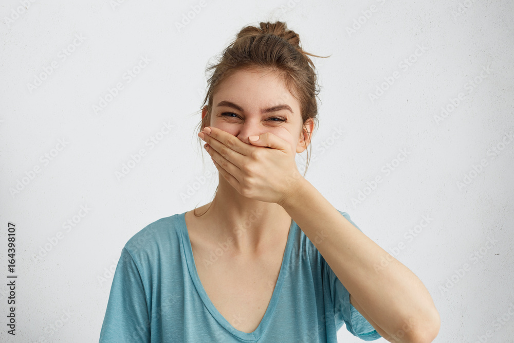 Positive female laughing while having good mood during spare time trying to control her emotions covering mouth with hand. Cheerful woman having fun bursting into laughing keeping hand on mouth