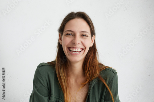 Positive European woman with long hair being glad to recieve congratulations with her birthday smiling pleasantly in camera posing against white studio wall. People, beauty, positive emotions concept