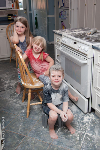  Three naughty children who have just made a mess in the kitchen sit beside the oven looking happy 