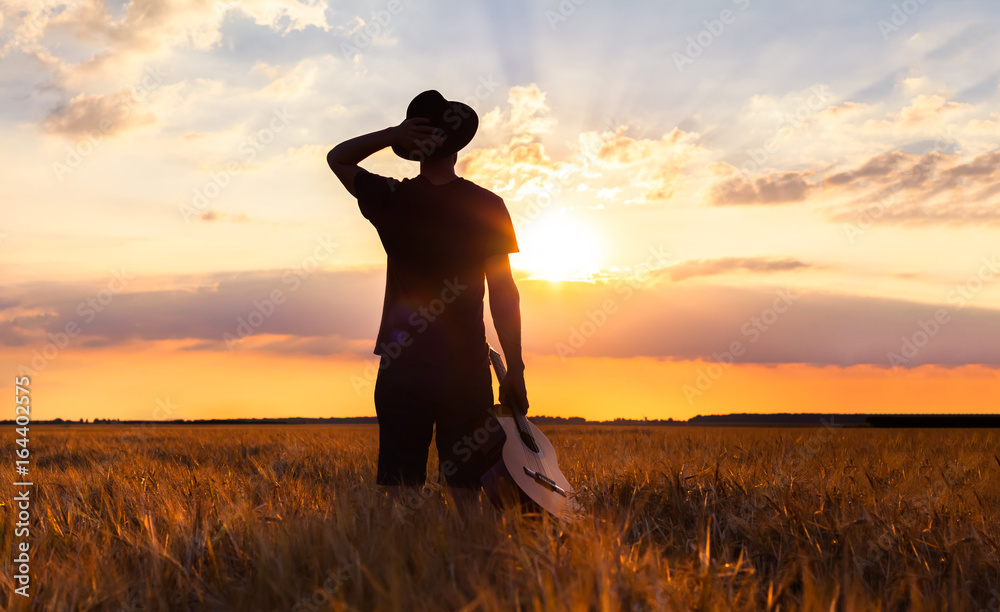 Person in warm summer fields with guitar, musician