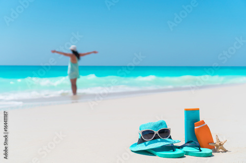 Beach accessories needed for sun protection with woman on background. Suncream bottles  goggles  starfish on white sand beach background ocean